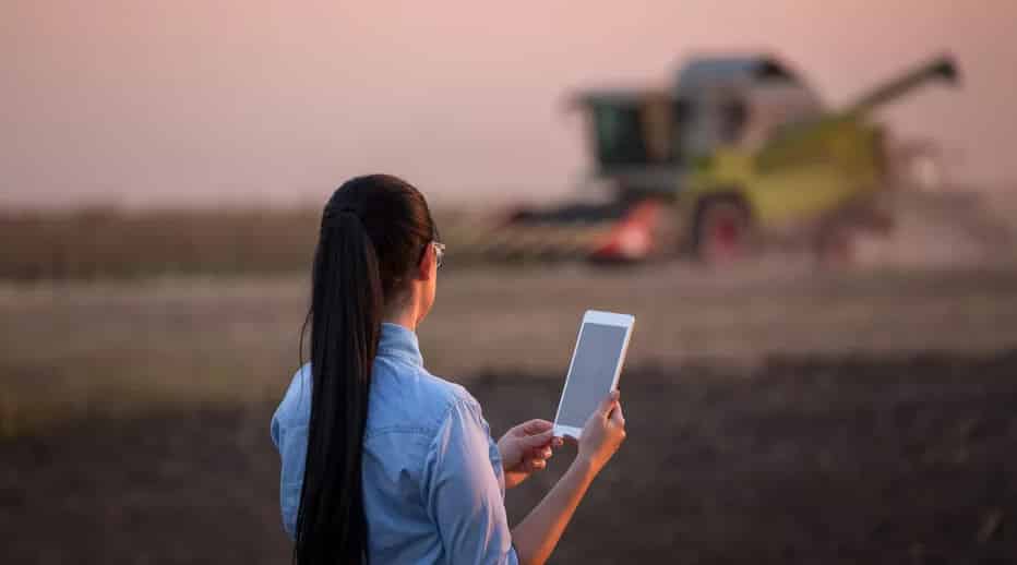 agricultora com ipad observando colheitadeira trabalhando