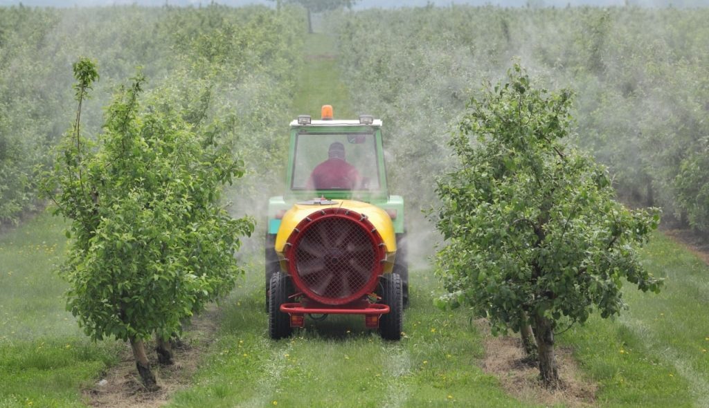 Trator puxando pulverizador com defensivos agrícolas aplicado em frutíferas