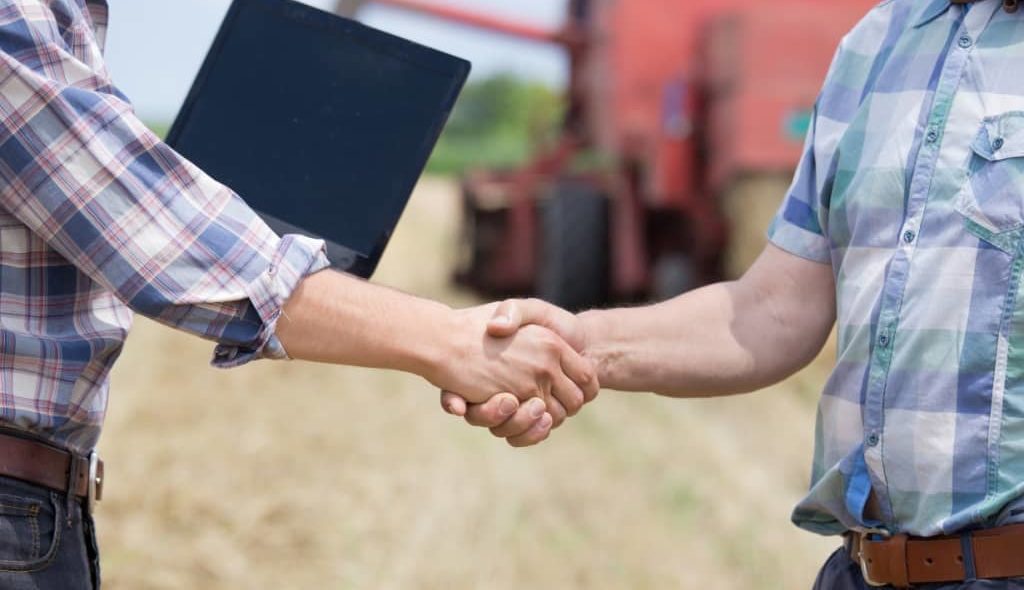 produtores dando as mãos com máquinas agrícolas ao fundo