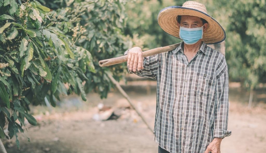 Agricultor com máscara segurando enxada na plantação