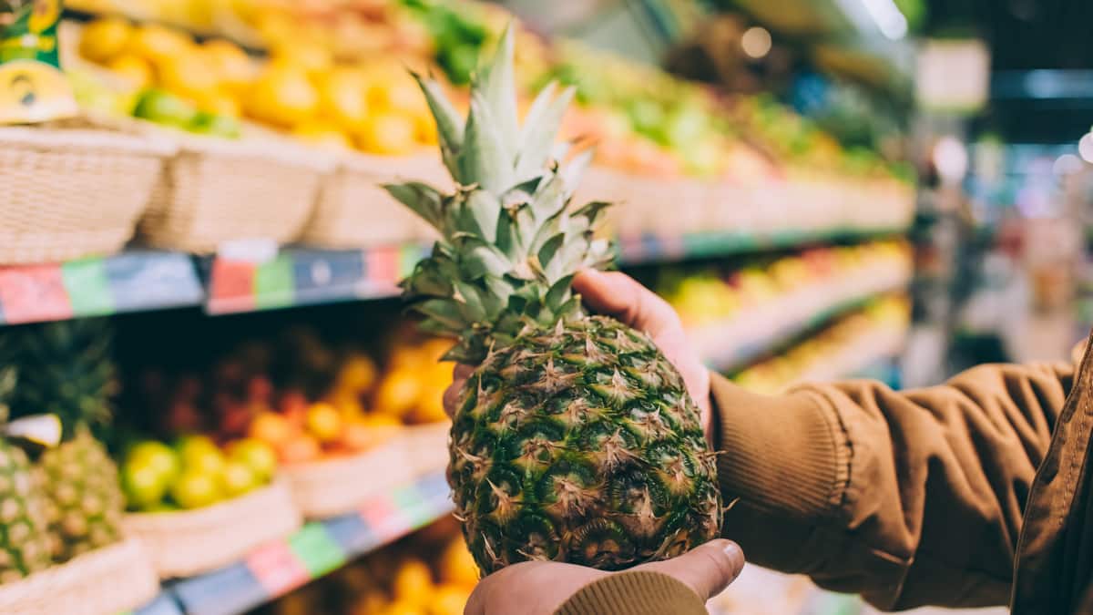 Homem segura abacaxi na seção de frutas de um supermercado