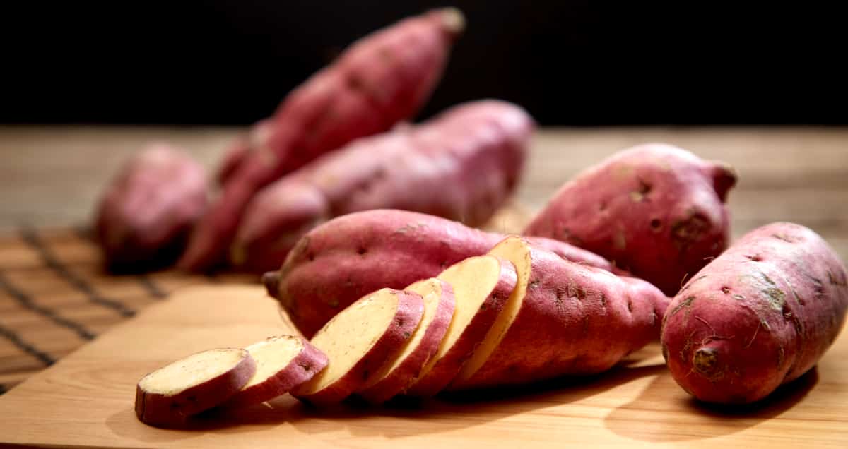 Algumas batatas-doce numa tábua, uma delas cortada em rodelas