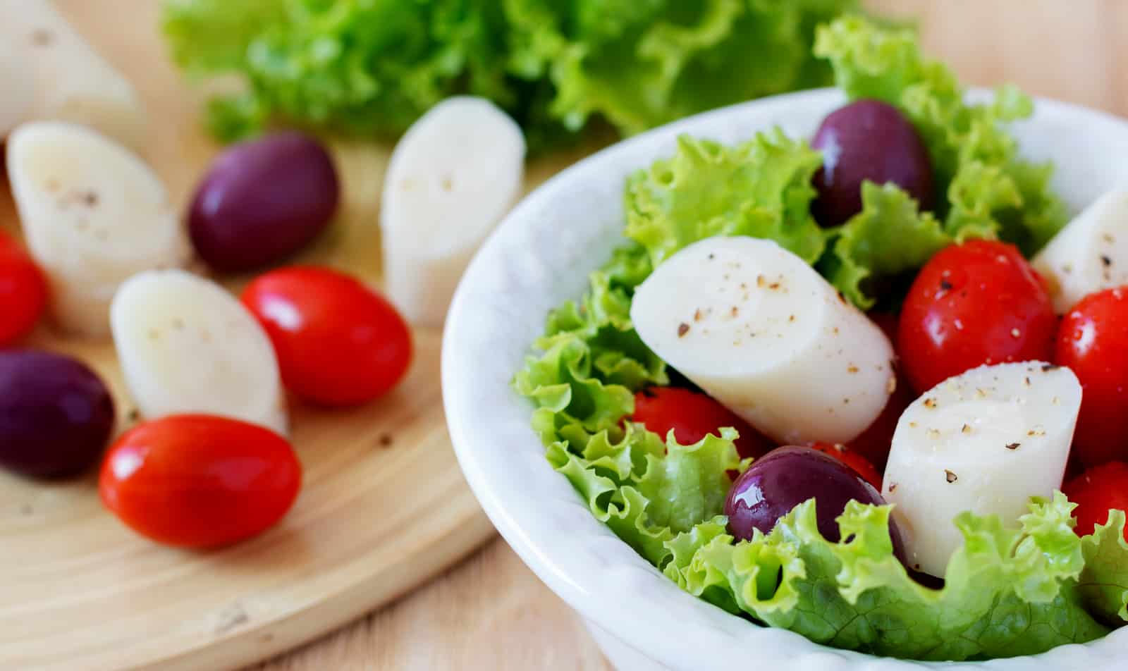 Vasilha branca com salada, contendo alface, tomate, azeitona e palmito