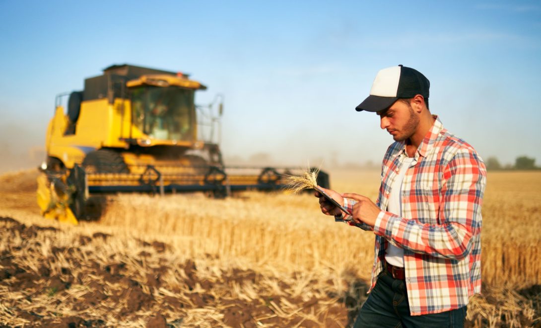 Homem com tablet na mão próximo à colhedora em campo de trigo
