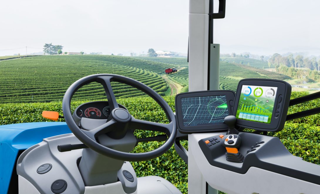Trator com tecnologia embarcada, mostrando o painel com monitores de agricultura de precisão. Ao fundo, campo verde.