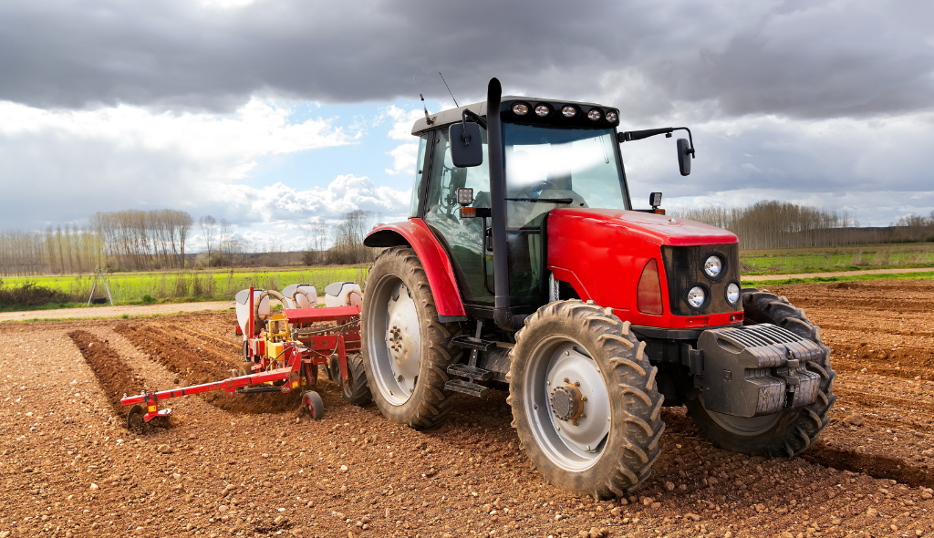 Trator moderno semeando o campo arado com equipamentos agrícolas.