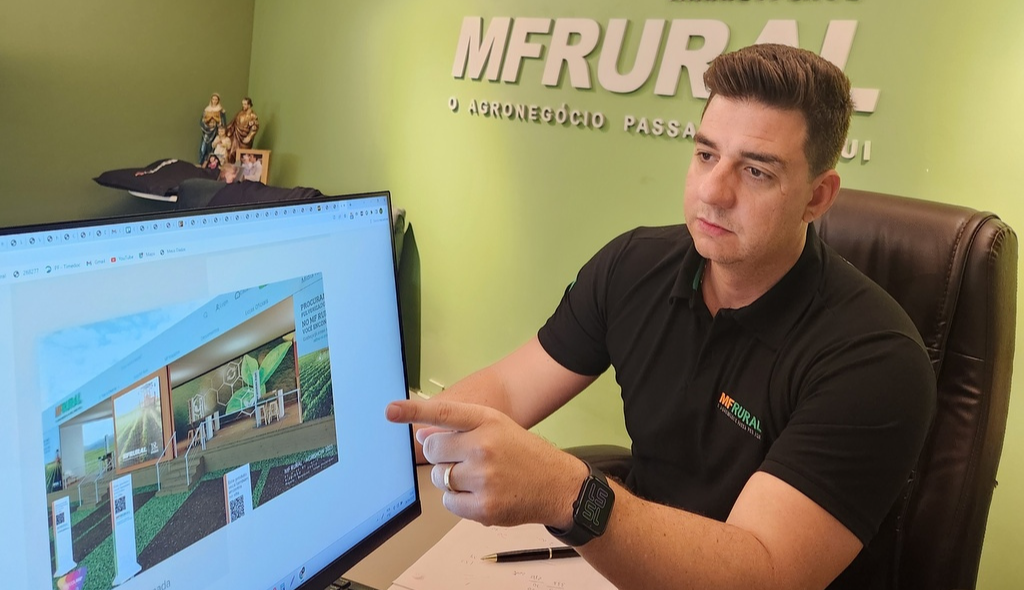 Rafael Lucas apontando para a tela do computador e mostrando uma foto do estande do MF Rural na Agrishow 2023.