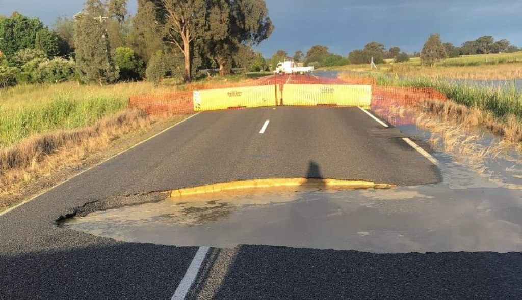 Parcela da estrada interditada por dano causado pelo não escoamento de água, resultando em um buraco que abrange as duas vias da pista