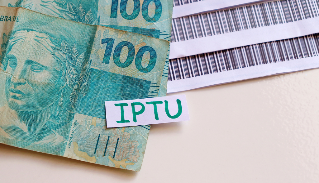 Notas de 100 reais e boletos sobre superfície lisa, com um pedaço de papel escrito IPTU
