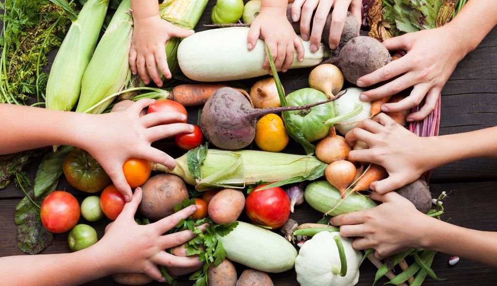 Foto de vegetais e legumes orgânicos sob as mãos de quatro crianças