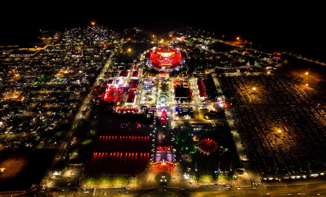 Vista aérea noturna do Parque do Peão de Barretos iluminado durante a Festa do Peão, com a arena, atrações e estacionamento ao redor.