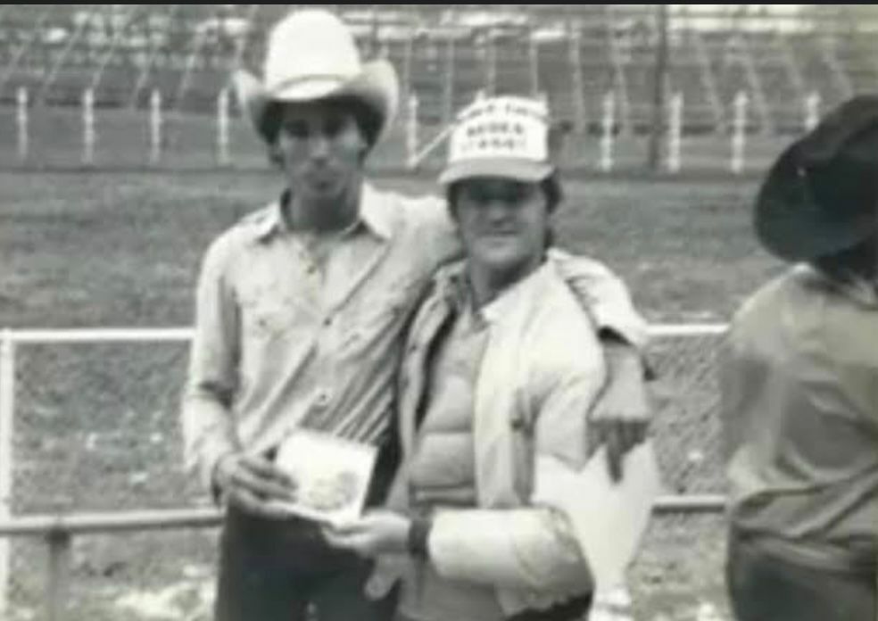 Tião Procópio aparece ao lado de seu instrutor, segurando a fivela de campeão da escola de rodeio nos Estados Unidos.